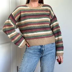 a woman standing in front of a door with her hands on her hips, wearing a multicolored sweater