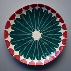 a red and green plate with white designs on it's rim, sitting on a gray surface