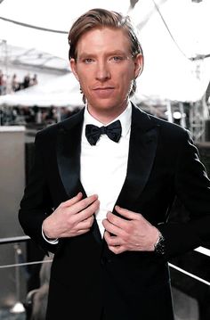 a man in a tuxedo is posing for the camera with his hands on his hips