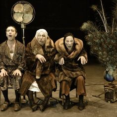 three people sitting in front of a peacock on a chair with a fan behind them