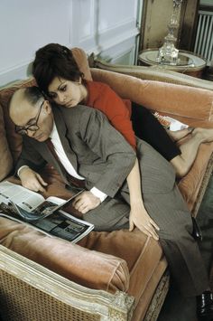 a man and woman are laying on a couch with an open magazine in their lap