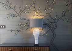 a lamp on a table next to a tree with blue and yellow flowers painted on it