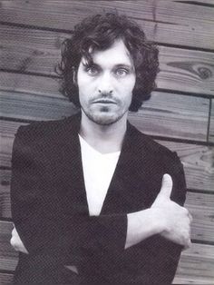 a man with his arms crossed posing for a photo in front of a wooden wall