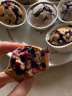 a person holding up a muffin with blueberries on it in front of other muffins