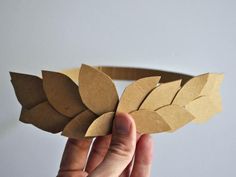 a person is holding up a paper leaf headband made out of brown paper and cardboard