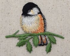 a small bird sitting on top of a green leafy branch embroidered onto a piece of fabric