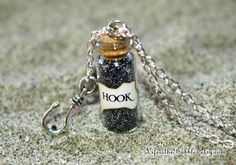 a bottle necklace with the word hook on it is sitting in the sand and has a chain attached to it