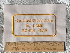 a piece of cloth with embroidered words on it and a ruler next to it that says quilted with love by name month year