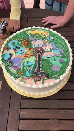 a cake that is sitting on top of a table with people around it and one person holding a cell phone