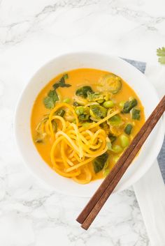 a bowl filled with noodles and vegetables next to chopsticks on a white surface