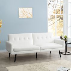 a white couch sitting on top of a wooden floor next to a vase filled with flowers