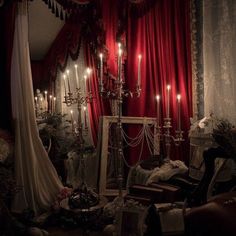 a room with red curtains and candles lit up in the dark, it looks like an old - fashioned bedroom