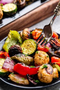 a fork is stuck into a plate of roasted vegetables with potatoes and zucchini