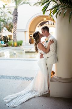 a bride and groom standing next to each other in front of a fountain with palm trees