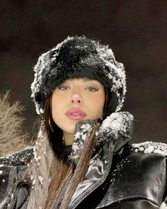 a woman wearing a black leather jacket and hat covered in snow with her eyes closed