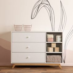 a white dresser sitting next to a wall with a plant on it's side