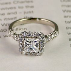 an engagement ring with a princess cut diamond surrounded by round brilliant diamonds on top of a sheet of paper