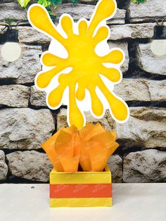 a paper cut out of an orange flower in a yellow vase on top of a table