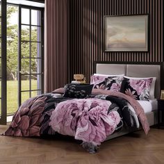 a bed with pink and black flowers on the comforter is in front of a window