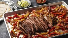 steak and peppers on a baking sheet with tortilla chips, lime wedges and salsa in the background