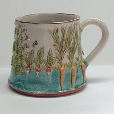 a ceramic mug with carrots and plants on it's side, sitting on a white surface