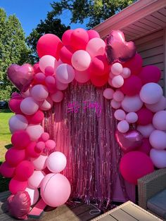 balloons and streamers are on the front door of a house with a pink backdrop