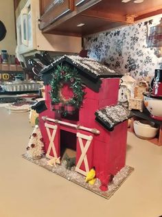 a small red house with a wreath on it's roof sitting on a kitchen counter