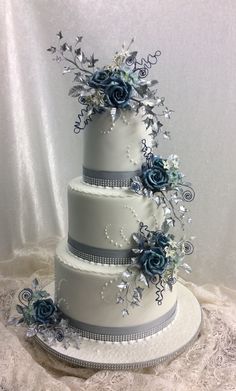 a three tiered white wedding cake with blue flowers on the top and silver ribbon