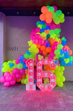 the number 16 is surrounded by balloons in front of a pink and purple wall with neon colors