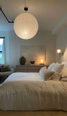 a large white bed sitting in a bedroom next to a window and lamp above it