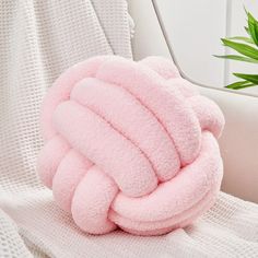 a pink pillow sitting on top of a white couch next to a potted plant