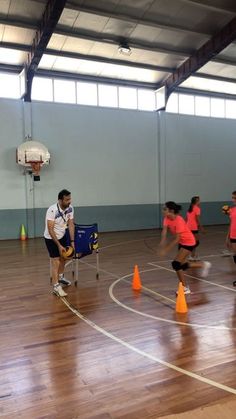 a group of people standing on top of a hard wood floored basketball court with orange cones