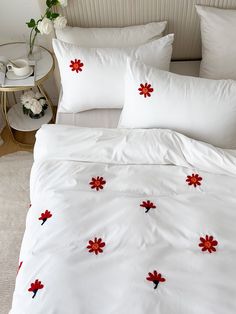 a bed with white sheets and red flowers on the pillow cases, along with two side tables