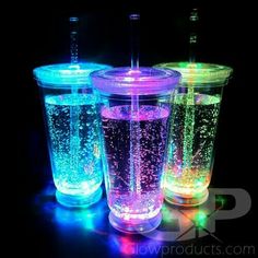 three different colored cups sitting next to each other on a black surface with lights in them