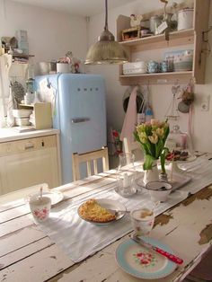 a table with plates and cups on it in a kitchen next to an old refrigerator