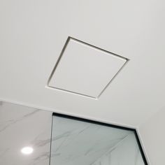 a bathroom with white walls and marble flooring, including a square light fixture on the ceiling