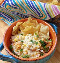 an orange bowl filled with mexican food and tortilla chips on top of a wooden table