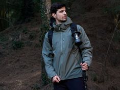 a man standing in the woods with a camera strapped to his back and holding a water bottle