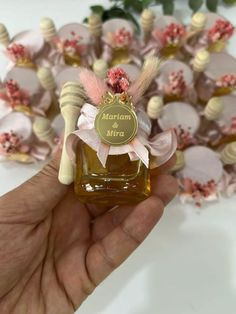 a hand holding a small bottle of honey with pink flowers in the background and a ribbon around it