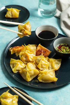 some dumplings on a black plate with chopsticks and dipping sauce in the bowl