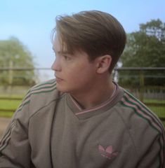 a young man sitting on top of a bench next to a green grass covered field