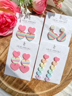 three pairs of heart shaped earrings sitting on top of a wooden table next to pink flowers