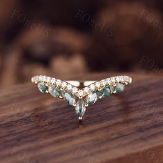 a gold ring with green and white stones sitting on top of a wooden table next to rocks