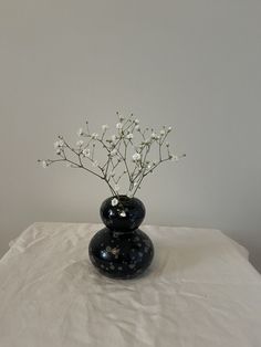 a black vase filled with white flowers sitting on top of a white cloth covered table