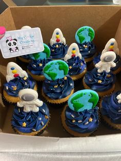 a box filled with blue cupcakes covered in frosting and space related decorations