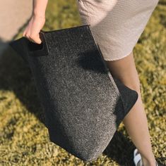 a woman carrying a black bag on top of grass covered ground with her foot in the air