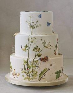 a three tiered cake with flowers and butterflies painted on the side, sitting on a platter