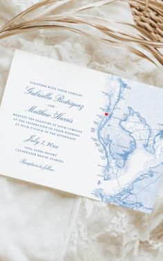 a wedding card with a map on it sitting on top of a white blanket next to a wicker basket