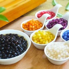 six bowls filled with different colored beans on top of a wooden table next to a plant