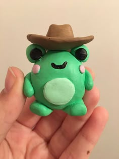 a hand holding a small green toy with a hat on it's head and eyes